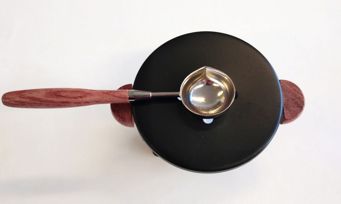 Sinettilakan sulatusalusta lusikalla, musta